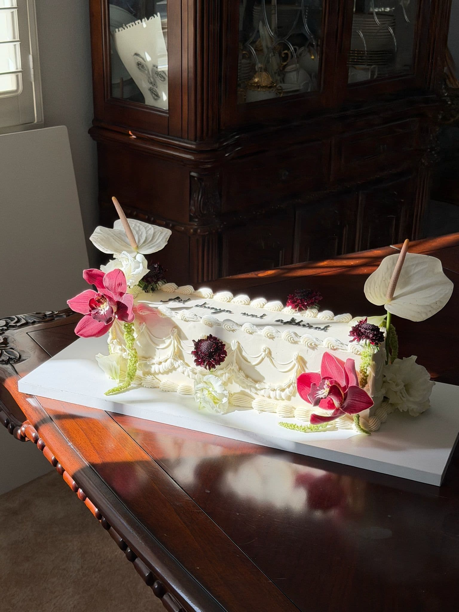 Vintage piped sheet cake in raking sunlight with anthuriums, orchids and dark scabiosa