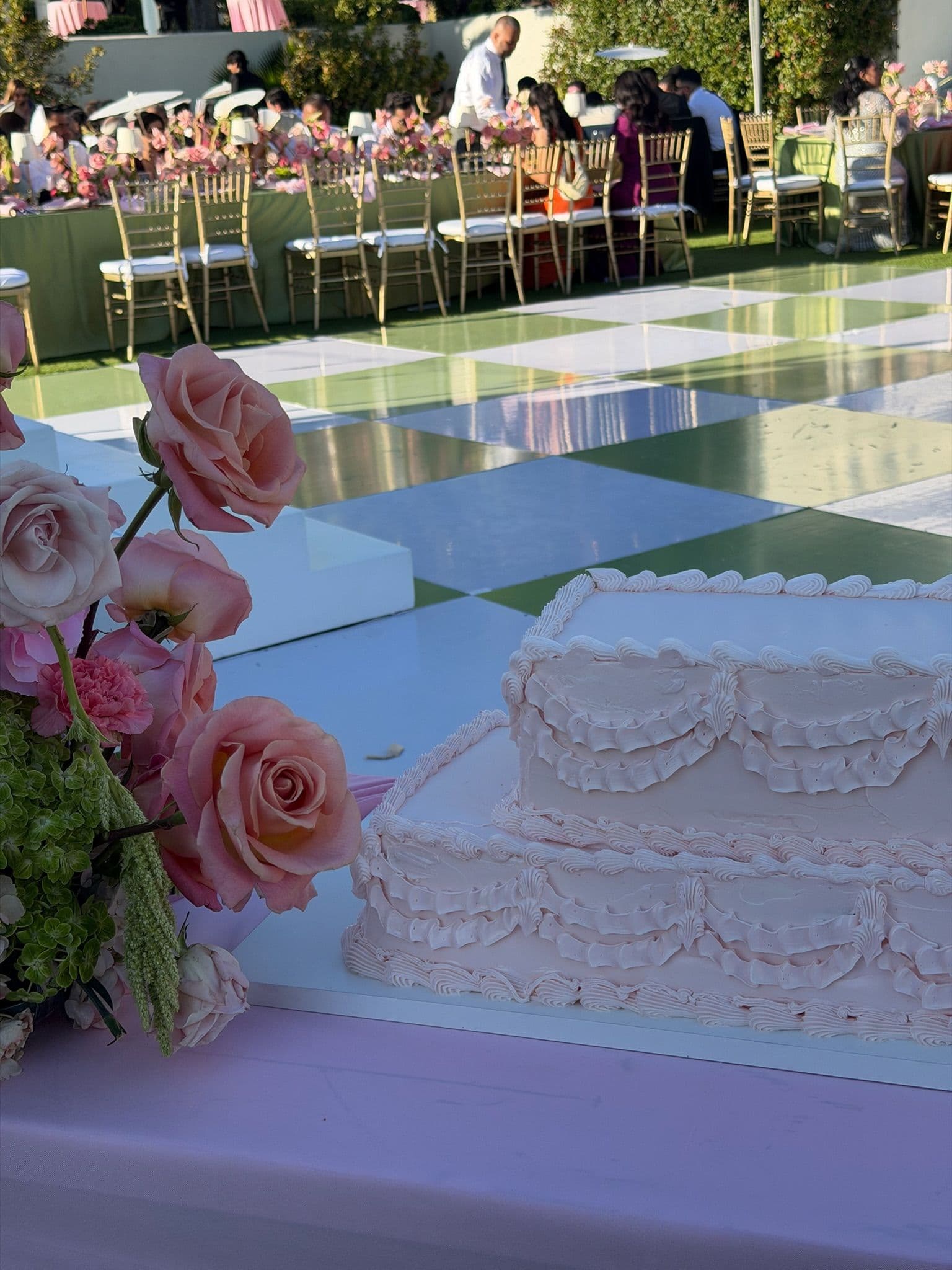 Blush tiered sheet cake with piped swags beside an arrangement of pink garden roses