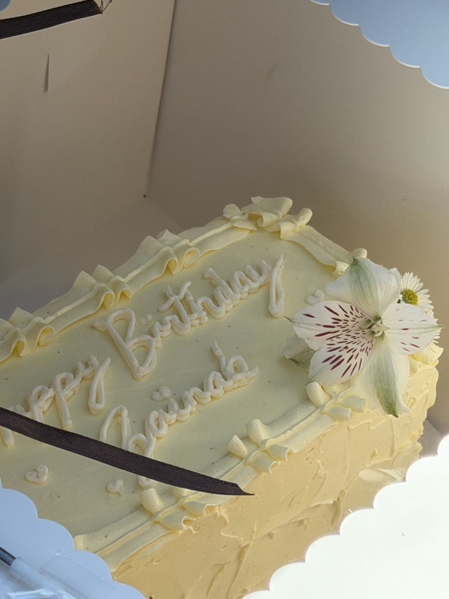 Ivory sheet cake with piped script and a single bloom, in a scalloped window box
