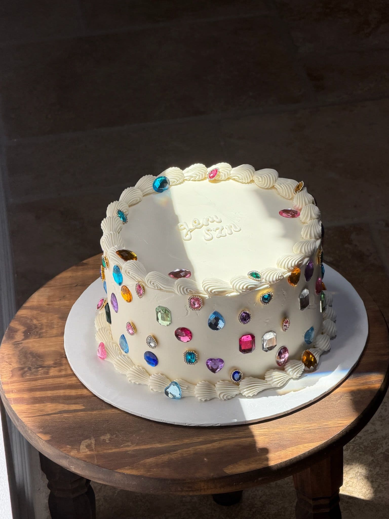 White cake scattered with jewel-toned buttercream dots and a piped plaque
