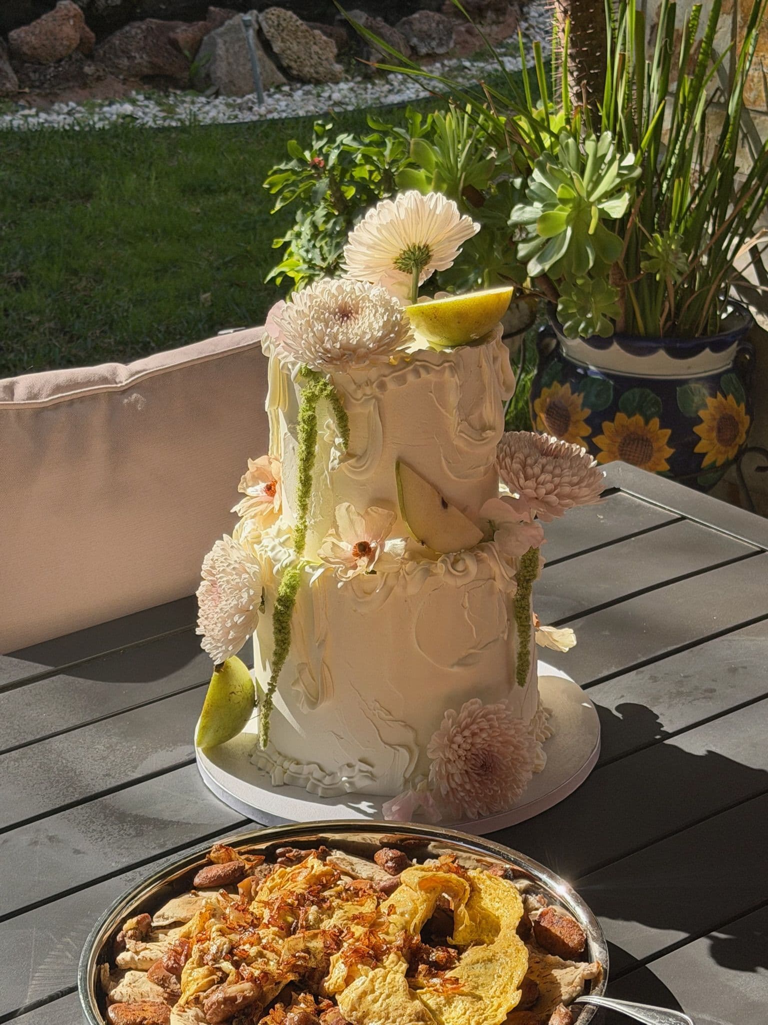Two-tier pear and chrysanthemum cake in hard afternoon light on a garden table