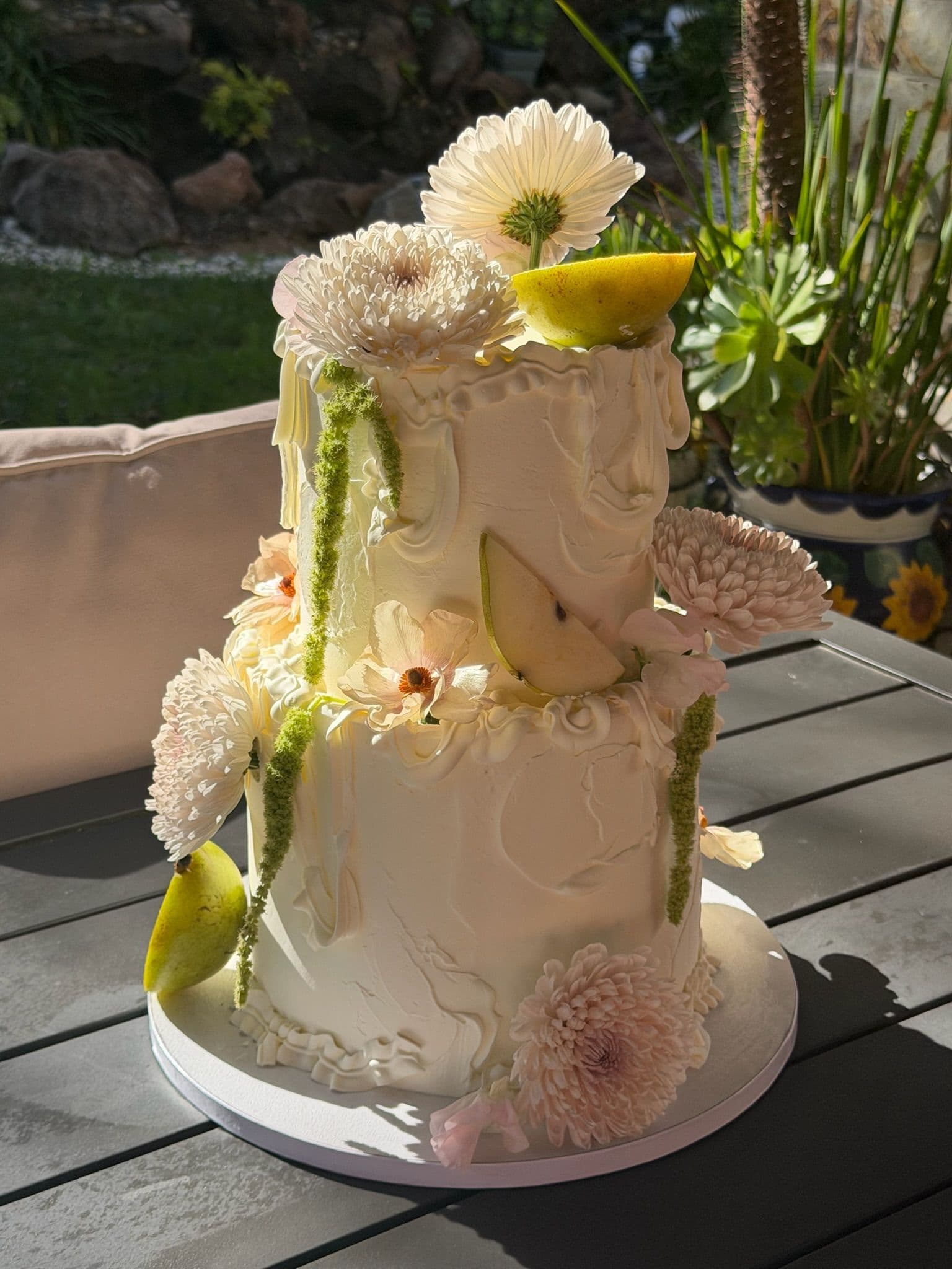 Two-tier buttercream cake with pear slices, cream chrysanthemums and amaranthus, in a garden