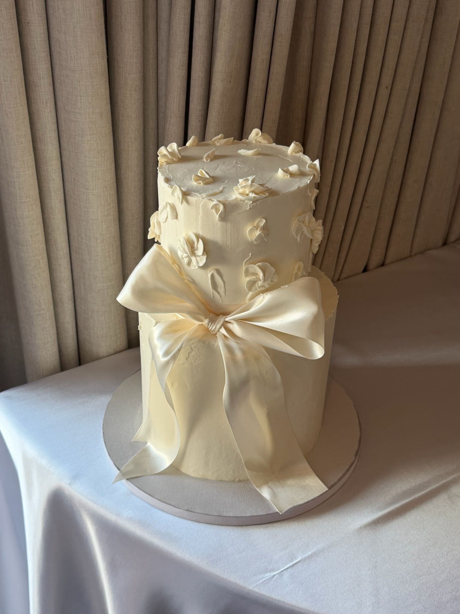 Tall ivory cake with piped blossoms, wrapped in a full cream satin bow
