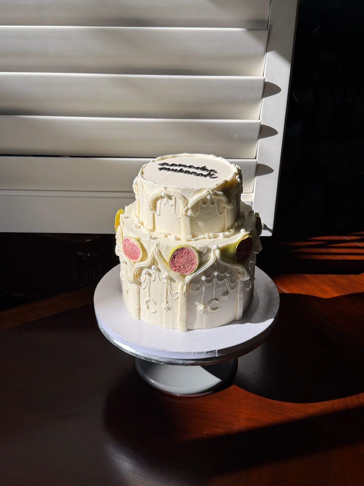 Two-tier cake with sculpted buttercream, pastel dots and a piped plaque