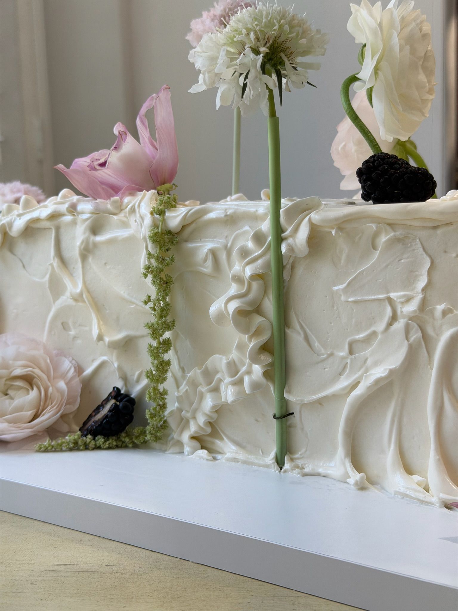 Close crop of hand-piped buttercream ruffles with pale florals and blackberries