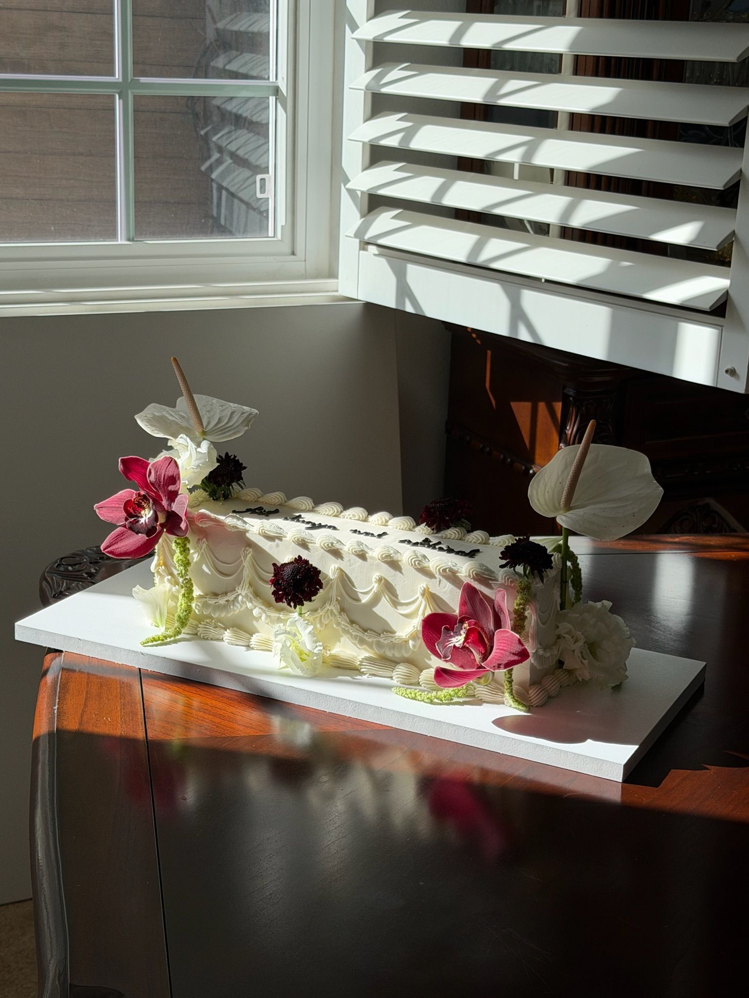 Long vintage-piped sheet cake with swag detailing, white anthuriums and deep pink cymbidium orchids