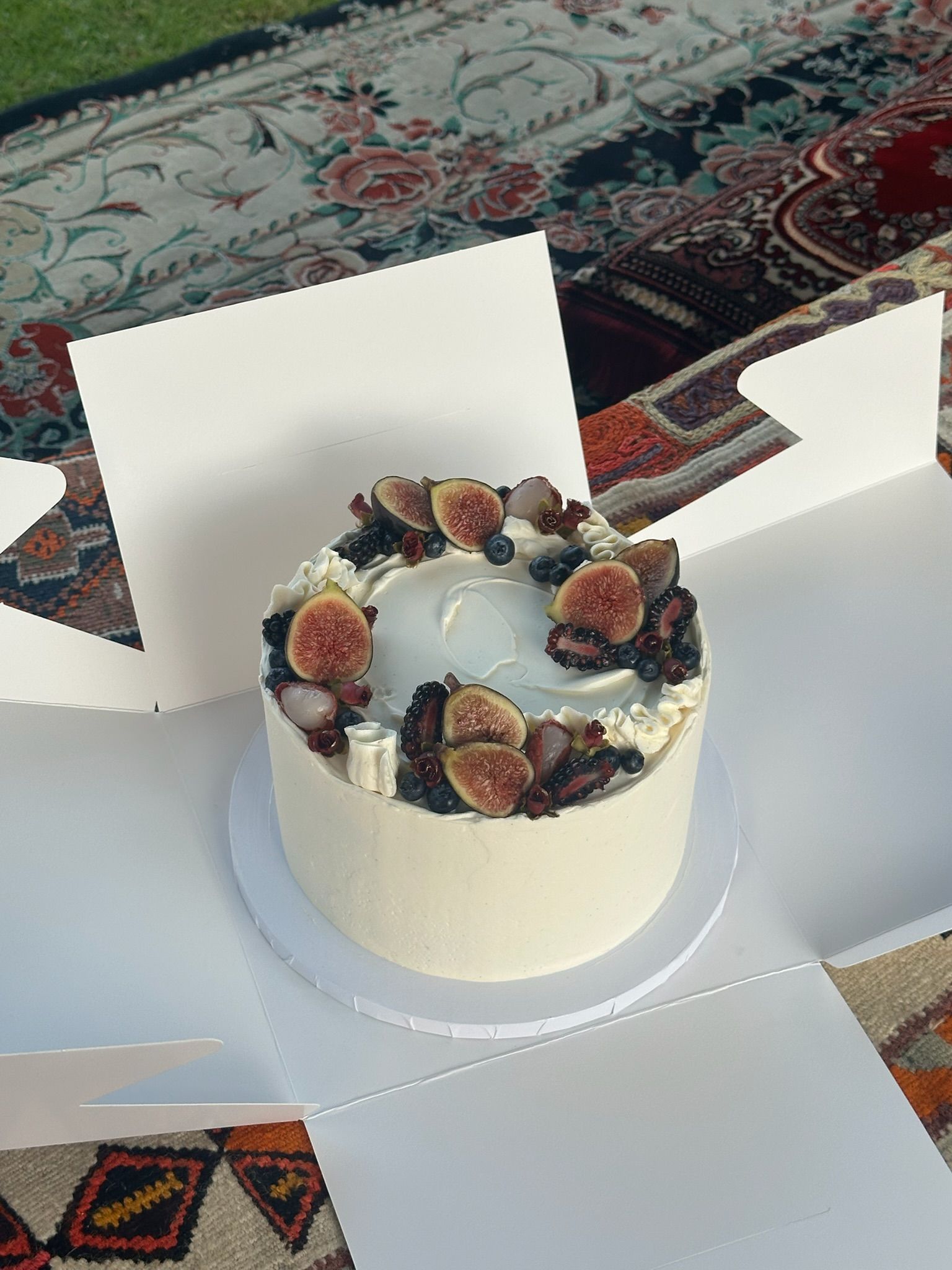 Cake crowned with halved figs, blackberries and blueberries, opened on a patterned rug