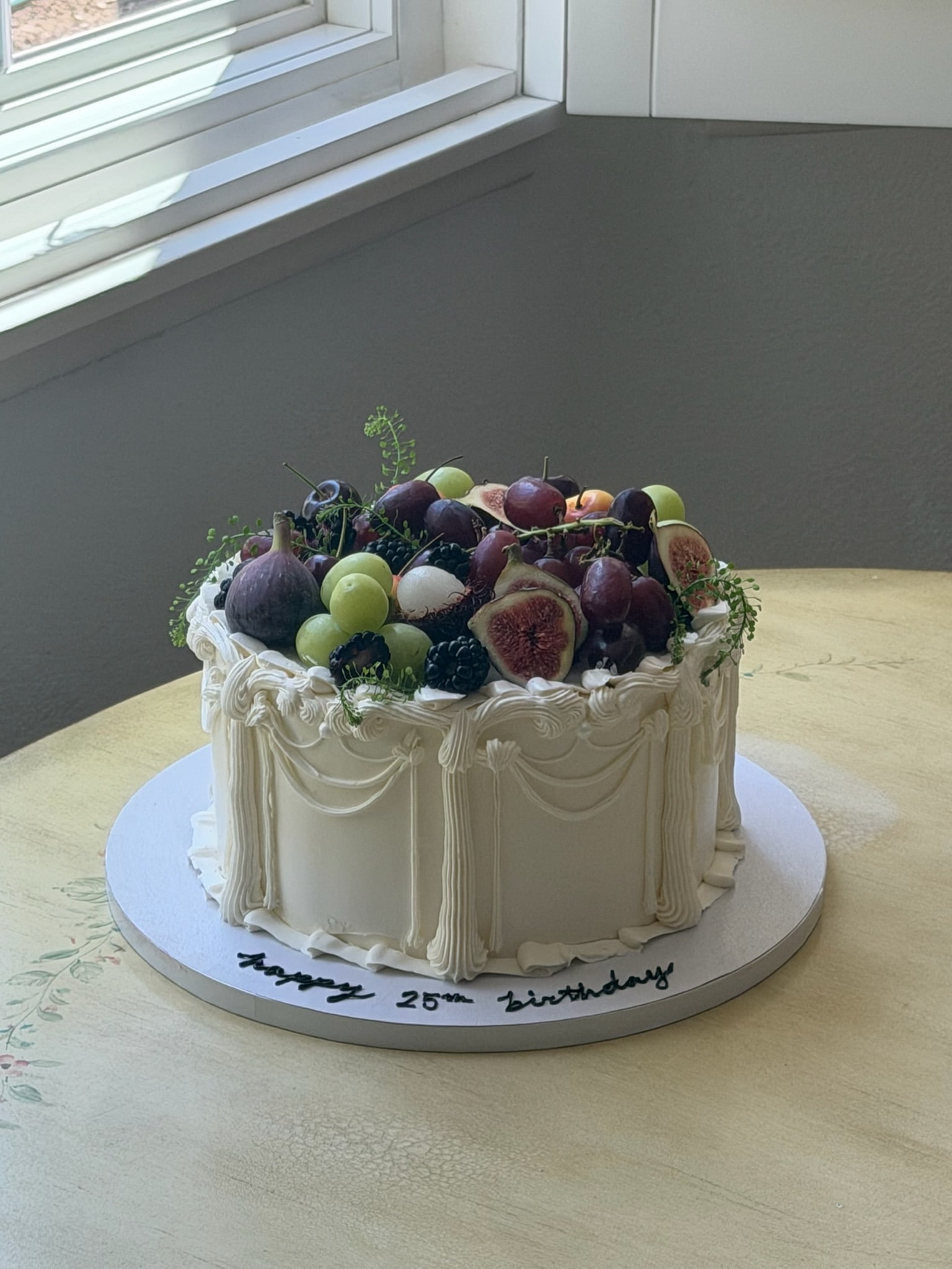 Round cake with draped piping, crowned with grapes, figs, blackberries and trailing greenery