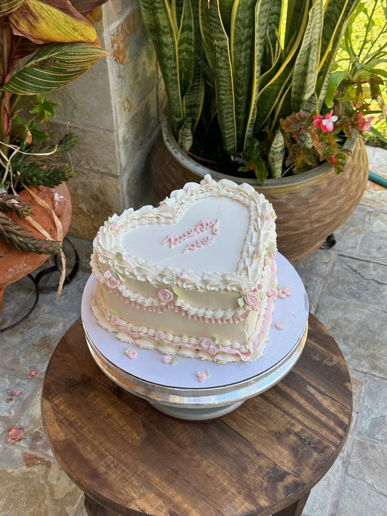 Heart-shaped cake with piped shell borders, pink rosebuds and a lettered heart plaque, on a cake stand
