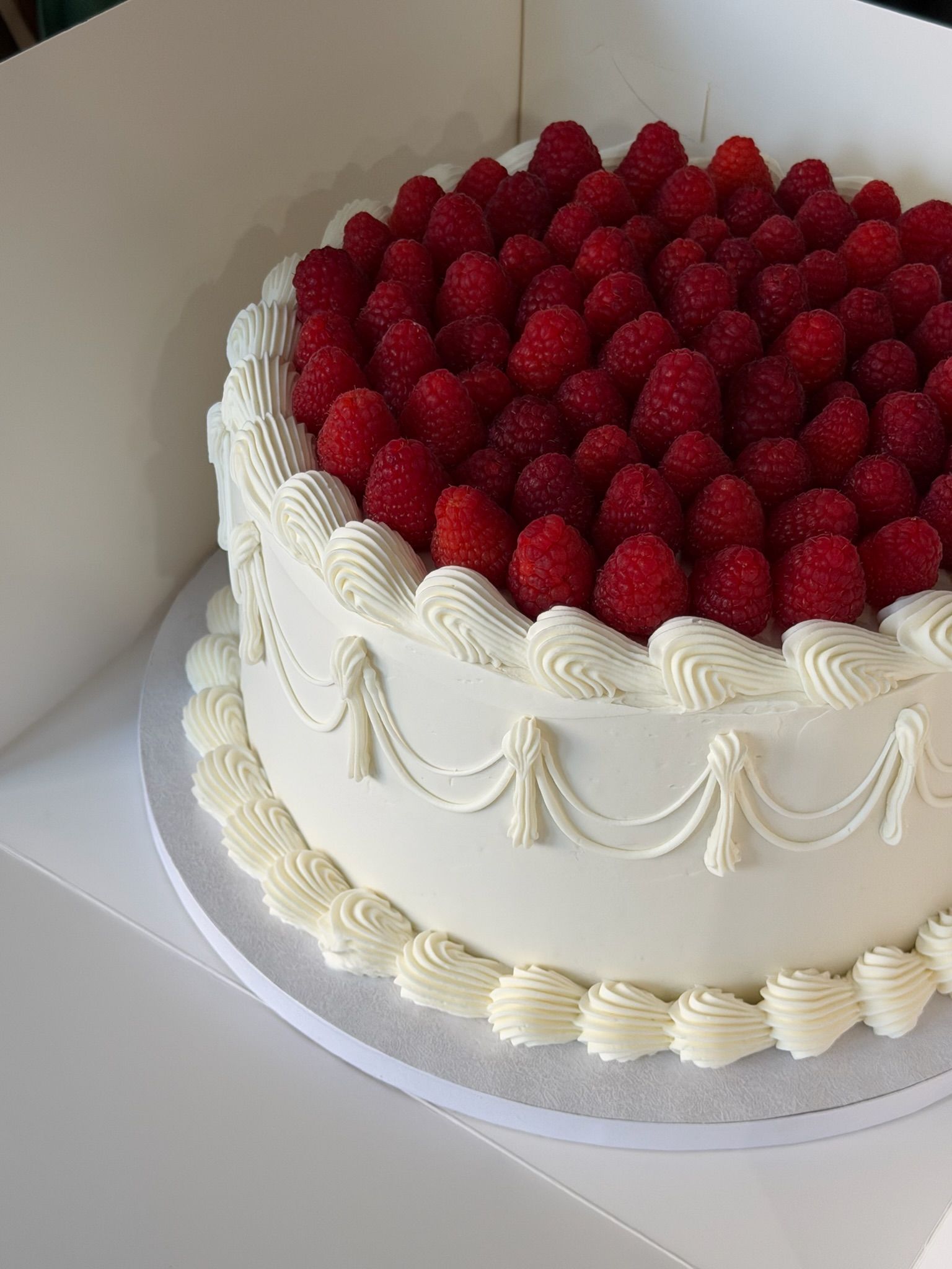 Vintage piped round cake with tassel swags and a dense crown of fresh raspberries