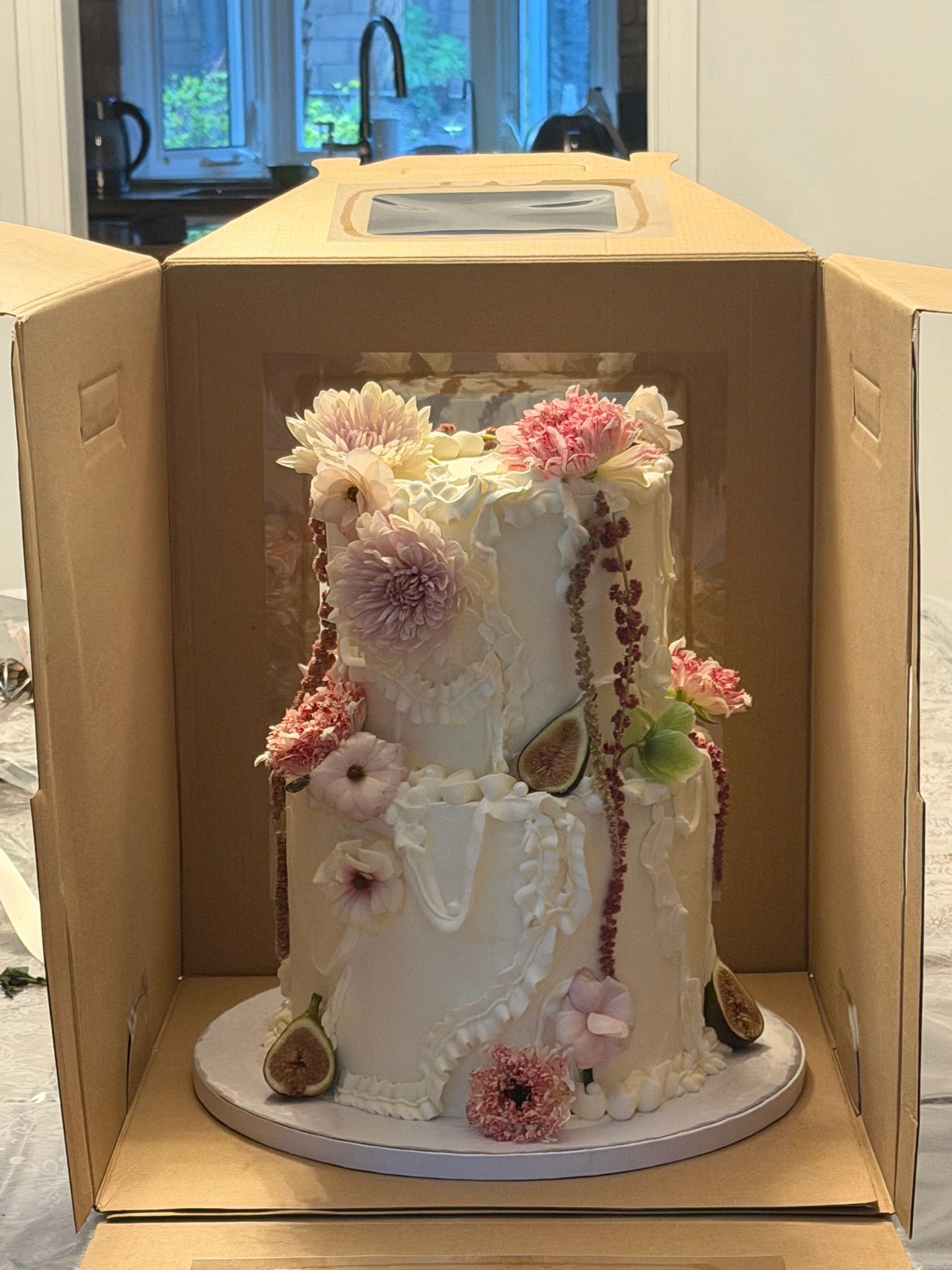 Two-tier textured cake with dahlias, blush blooms and figs, boxed for transport