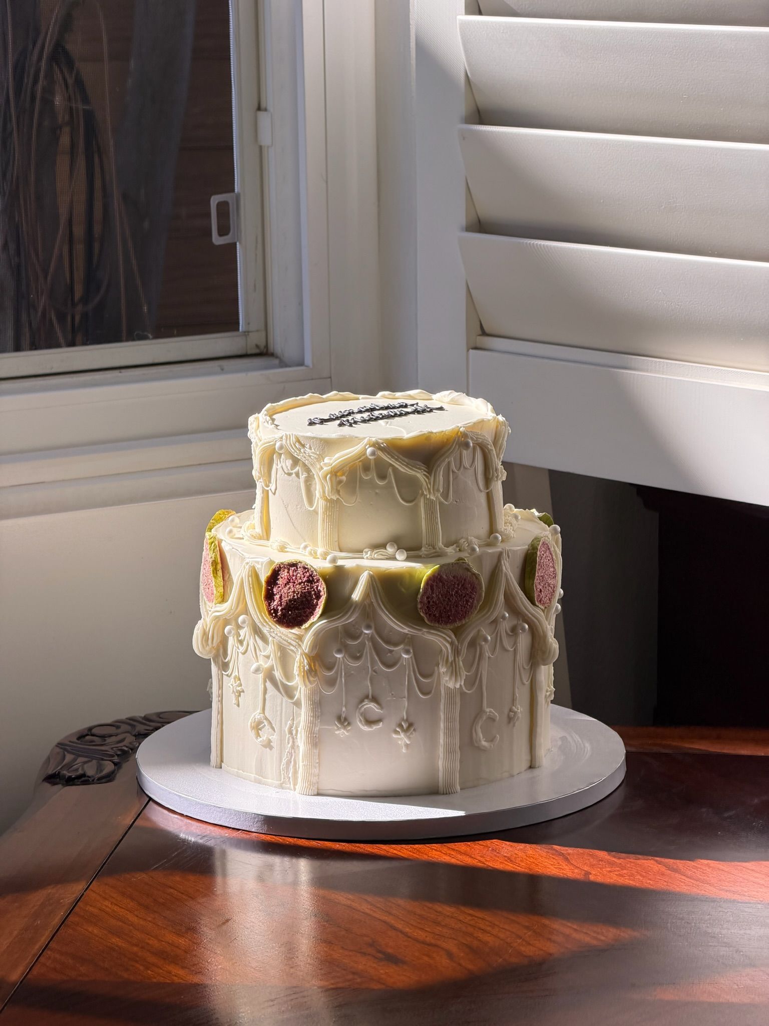 Two-tier cake with gothic piped arches, pearls and freeze-dried figs, in warm window light